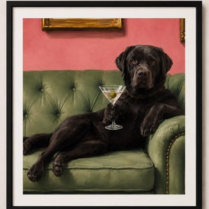 May include: A framed wall art print featuring a black Labrador retriever sitting on a tufted green leather sofa. The dog holds a martini glass with a single green olive in its paw. The background is a solid pink wall with gold frames.