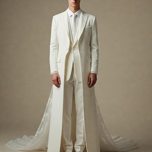 May include: A white three-piece suit featuring a long, floor-length coat with a structured collar, a matching vest, a crisp white dress shirt, a white necktie, and tailored trousers. The coat includes a long, sheer, lace-trimmed train.