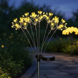 May include: A solar-powered garden stake light featuring a cluster of thin, metallic stems topped with small, glowing warm yellow LED bulbs. The fixture includes a circular solar panel mounted on a central pole, designed for outdoor ground installation.