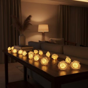 Puede incluir: Una guirnalda de luces LED decorativas con múltiples cubiertas en forma de rosas blancas. Cada rosa emite un brillo cálido y suave, conectadas por un cable fino. Las luces están dispuestas en línea sobre una superficie de madera oscura.