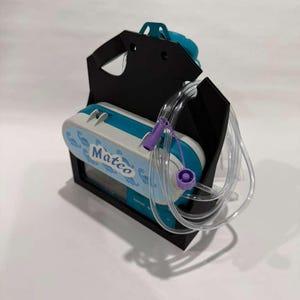 May include: A medical device labelled "Mateo", in blue and white, held in a black carrier. Clear tubing with purple connectors is attached. The device is designed for medical use.