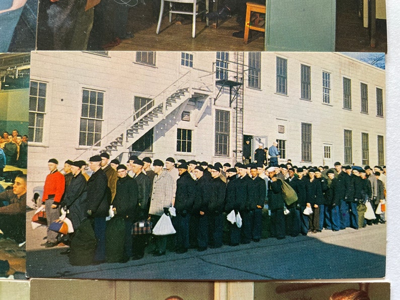 May include: A black and white photograph of a group of men in uniform standing in a line in front of a building. The men are wearing black hats and dark jackets. The building is a large, white building with many windows.