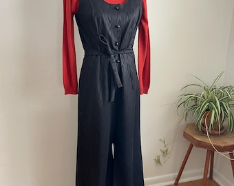 May include: A vintage black jumpsuit with a sleeveless top and wide legs. The jumpsuit features a tie belt and button details. A red turtleneck sweater is worn underneath. The outfit is displayed on a mannequin.