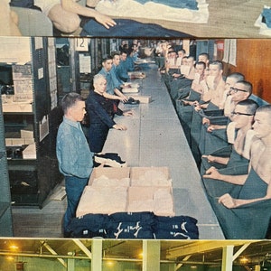 May include: A group of men in a factory setting are folding dark blue fabric. The men are shirtless and wearing dark blue towels around their waists. A man in a light blue shirt is standing at a table with boxes of fabric.