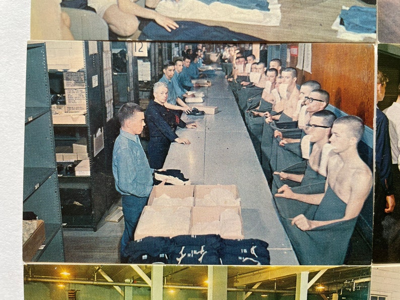 May include: A group of men in a factory setting are folding dark blue fabric. The men are shirtless and wearing dark blue towels around their waists. A man in a light blue shirt is standing at a table with boxes of fabric.