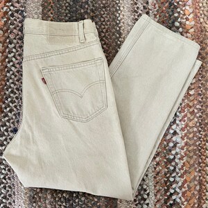 May include: A pair of light beige denim jeans with a red Levi's logo on the back pocket.