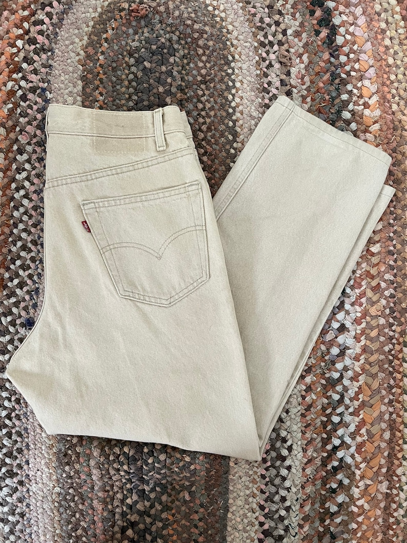 May include: A pair of light beige denim jeans with a red Levi's logo on the back pocket.