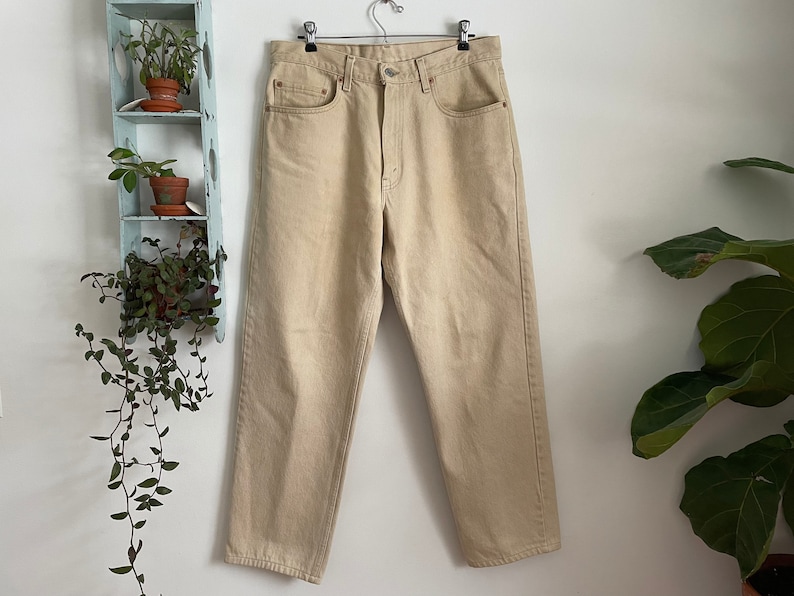 May include: A pair of light beige, straight-leg jeans with a high waist and five pockets.