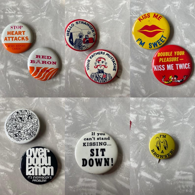 May include: A collection of vintage button pins with various designs and slogans. The pins feature colorful graphics and text, including "Stop Heart Attacks", "Red Baron", "Hello Stranger", "Kiss Me I'm Sweet", "Your Fathers Mustache", "Double Your Pleasure - Kiss Me Twice", "Help", "Over Population It's Everybody's Problem", "If You Can't Stand Kissing... Sit Down", and "I'm A Browser".