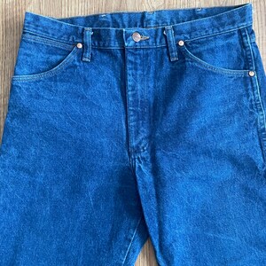 May include: A pair of dark blue denim jeans with a button fly and five pockets.