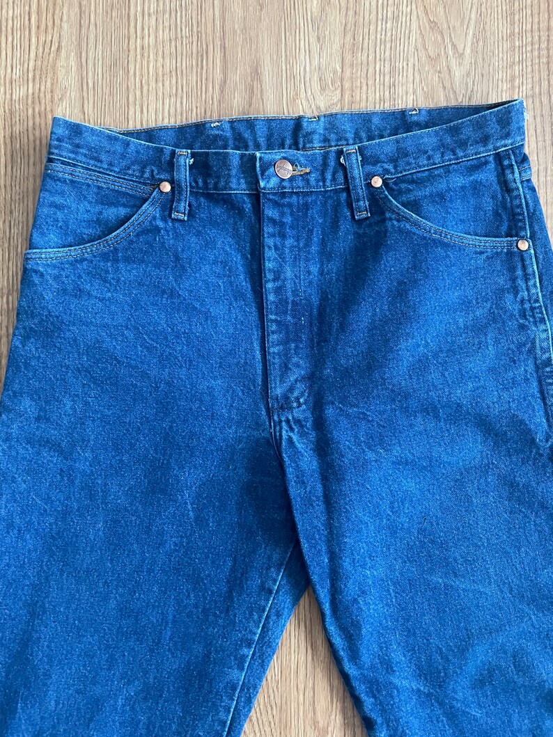 May include: A pair of dark blue denim jeans with a button fly and five pockets.