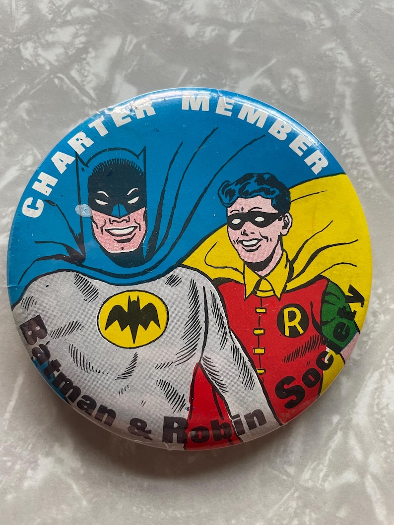 May include: A blue, yellow, and red round button with a picture of Batman and Robin. The text on the button reads "Charter Member Batman & Robin Society".