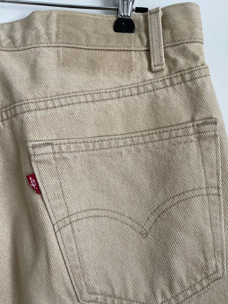 May include: A pair of beige denim jeans with a red Levi's patch on the back pocket.