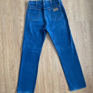 May include: A pair of dark blue denim jeans with a brown leather patch on the back pocket that says "Wrangler".