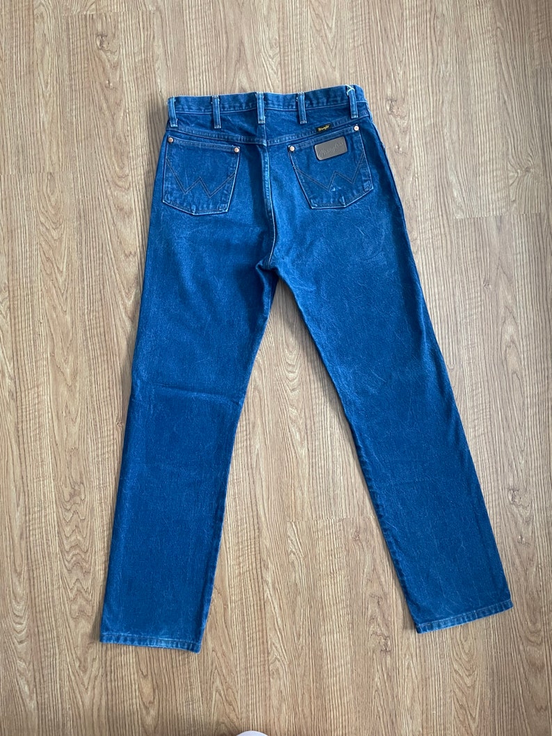 May include: A pair of dark blue denim jeans with a brown leather patch on the back pocket that says "Wrangler".