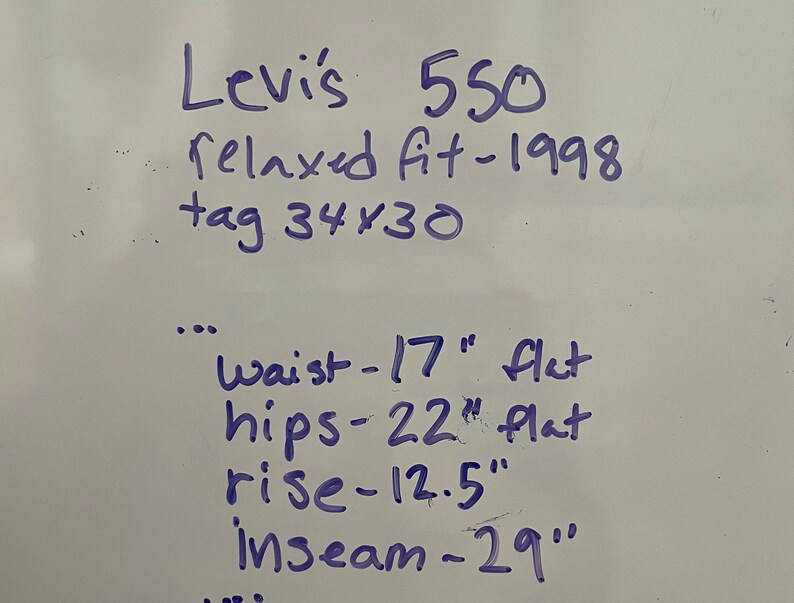 May include: Handwritten notes on a white surface, detailing the measurements of a pair of Levi's 550 relaxed fit jeans. The measurements include waist, hips, rise, and inseam in inches. The tag size is 34x30 and the jeans are from 1998.