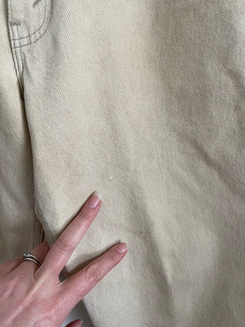 May include: Close-up of a pair of light beige denim pants. The fabric has a subtle texture and a slight sheen.