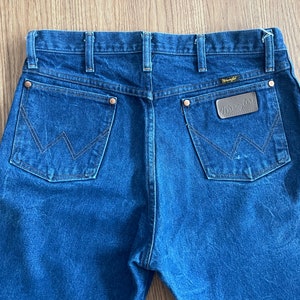May include: A pair of blue denim jeans with a brown leather Wrangler patch on the back pocket.