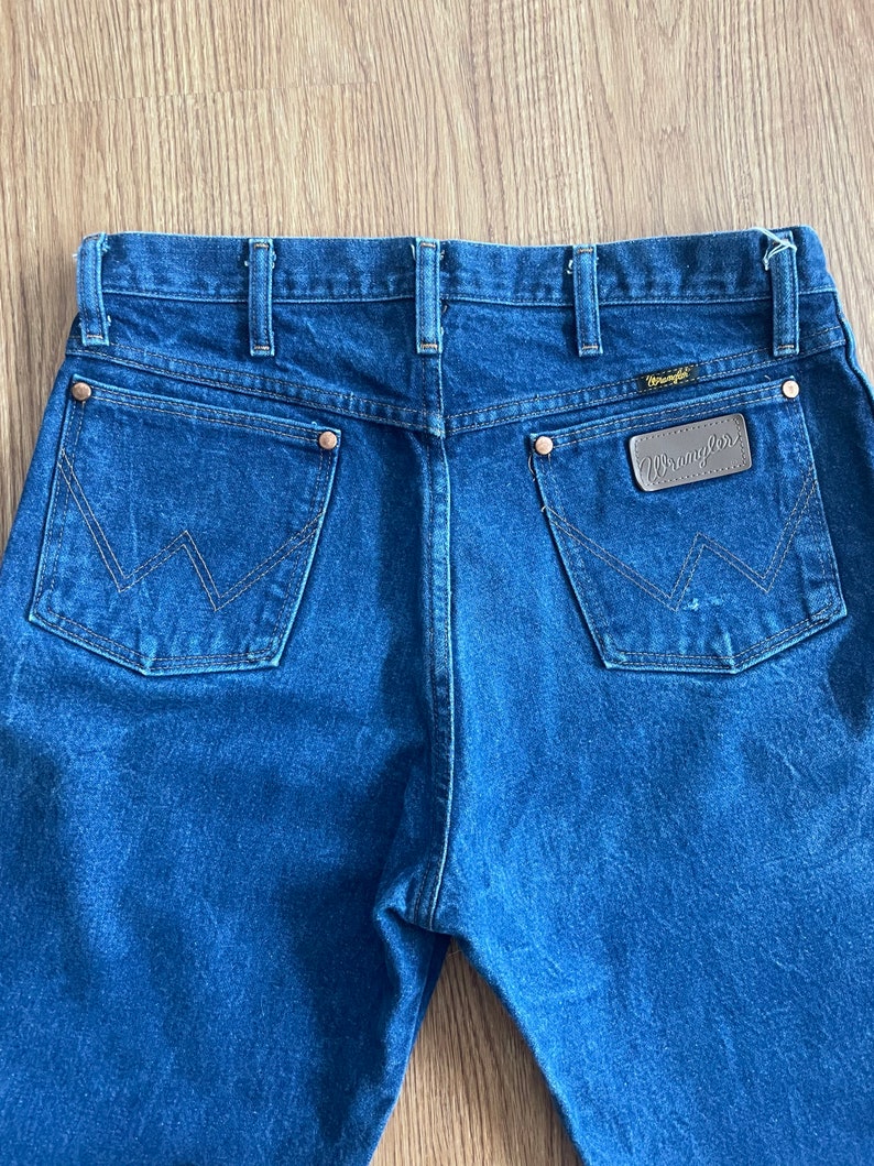 May include: A pair of blue denim jeans with a brown leather Wrangler patch on the back pocket.