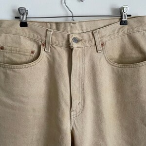 May include: A pair of light beige denim jeans with a classic five-pocket style. The jeans have a straight leg and a relaxed fit.