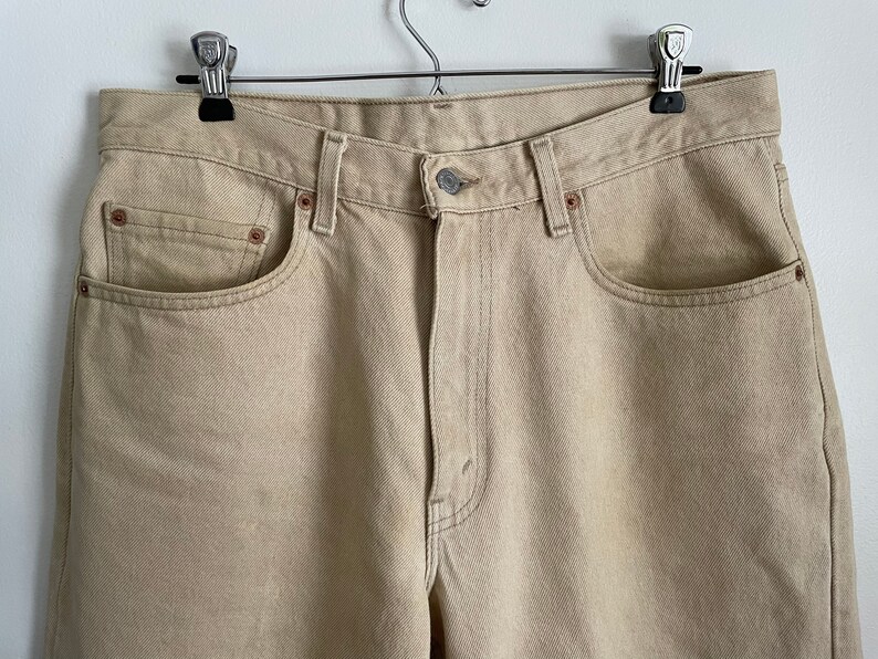 May include: A pair of light beige denim jeans with a classic five-pocket style. The jeans have a straight leg and a relaxed fit.