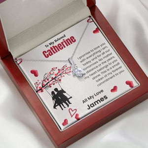 May include: A silver-toned necklace with a clear crystal pendant resting on a white card inside a dark wood box. The card features the text To My Beloved Catherine, a silhouette of two people on a swing, and a message signed by James.
