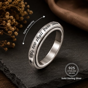 Peut inclure: Une bague rotative en argent gravée du texte This too shall pass et d'un symbole de flèche. La bague porte les mentions 925 Sterling Silver et Solid Sterling Silver. Un graphique avec le texte Spins smoothly indique le mouvement.