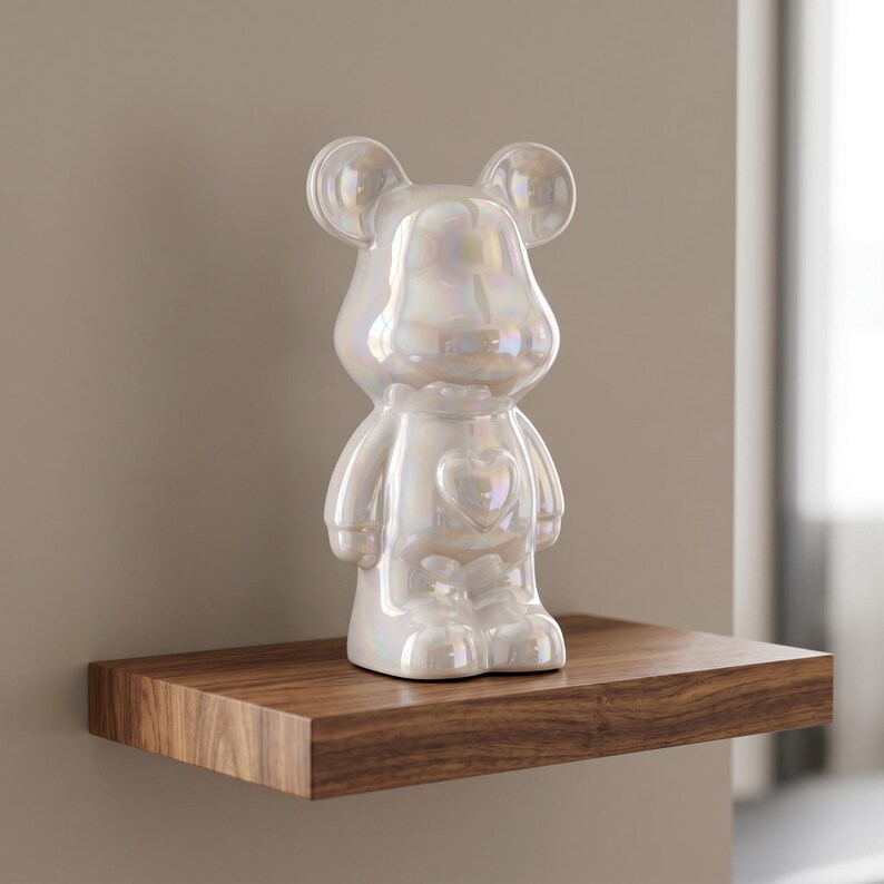 May include: A standing bear-shaped figurine with a smooth, iridescent, pearlescent finish. The figure features rounded ears, a prominent heart-shaped detail centered on the chest, and a stylized, smooth body design with defined limbs and feet.