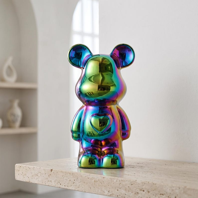 May include: A bear-shaped figurine with a reflective, iridescent finish that shifts between shades of green, blue, purple, and gold. The figure features rounded ears, a smooth surface, and a prominent heart-shaped indentation on the chest.