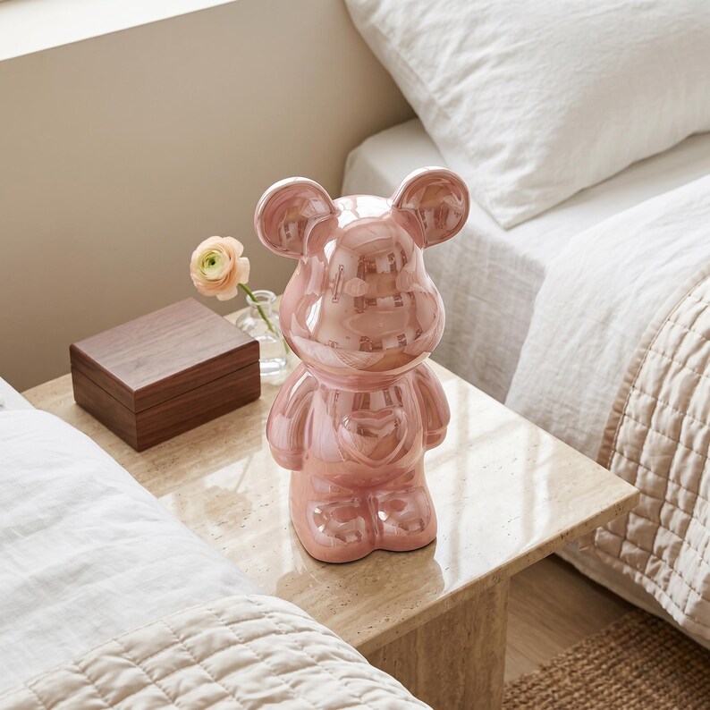 May include: A glossy, metallic rose-gold ceramic bear figurine featuring a smooth, reflective surface and a prominent heart shape embossed on its chest. The bear has rounded ears, a rounded snout, and a standing posture with arms at its sides.