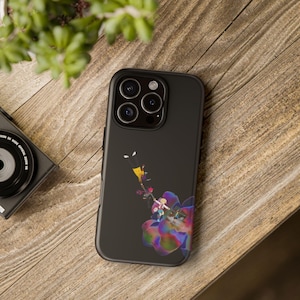 以下が含まれることがあります： マットブラックのスマートフォンケース。大きなカラフルで虹色に輝く花の上で、二人の人物が互いに手を伸ばしているグラフィックイラストが描かれています。デザインはケース背面の中央に配置され、トリプルレンズカメラ用の切り抜きがあります。