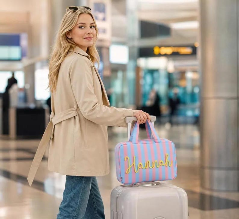 May include: A rectangular travel bag featuring vertical light blue and pink stripes with the name Hannah written in yellow cursive script on the front. The bag has two top handles and is positioned on top of a light gray rolling suitcase.