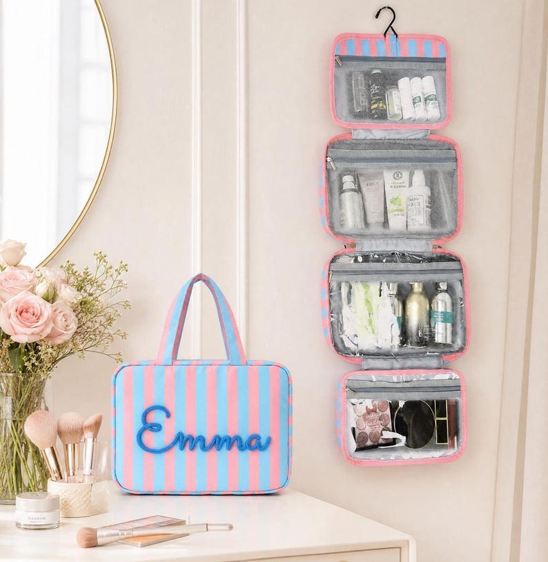 May include: A hanging toiletry bag with four clear zippered compartments and a matching rectangular travel case, both featuring pink and blue vertical stripes. The travel case displays the name Emma in blue script lettering on the front.