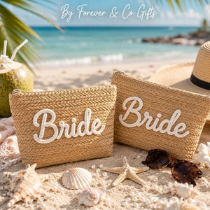 May include: Two tan woven straw pouches featuring the word Bride in white cursive lettering. The pouches are displayed alongside a straw hat, a coconut, a starfish, seashells, and sunglasses on a sandy beach with the text By Forever & Co Gifts.