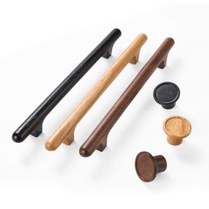May include: A collection of wooden cabinet hardware including three long, cylindrical bar pulls and three round knobs. The items are finished in three distinct wood tones: a deep black, a natural light oak, and a rich, dark brown walnut finish.