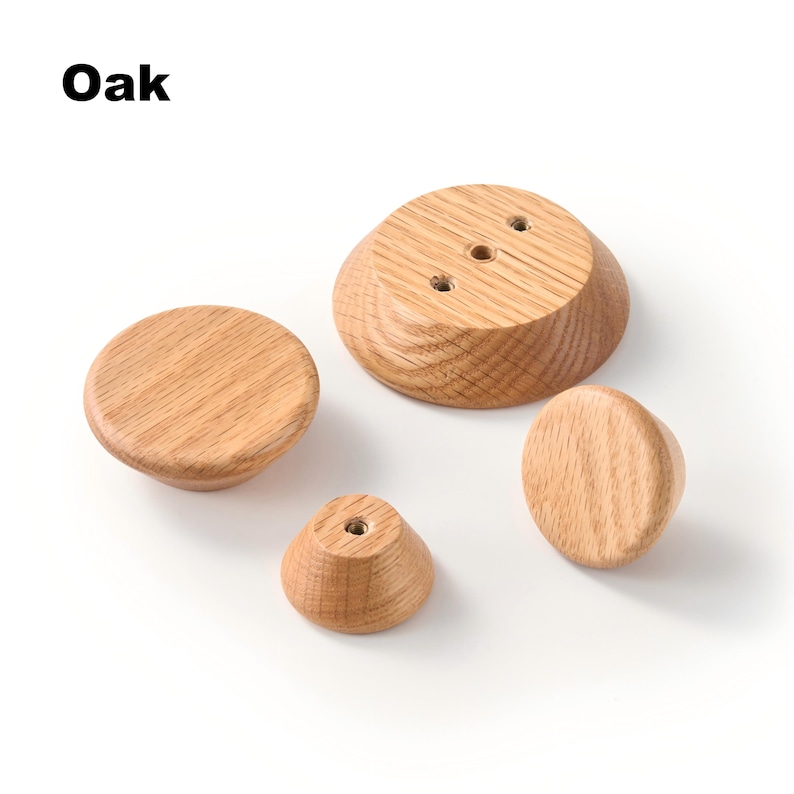 Op de afbeelding: Vier ronde eikenhouten knoppen van verschillende groottes, met een natuurlijk lichtbruin houtnerfpatroon. De tekst "Oak" is zichtbaar in de linkerbovenhoek. Sommige knoppen tonen een plat bovenoppervlak, andere onthullen een metalen schroefdraadinzet.