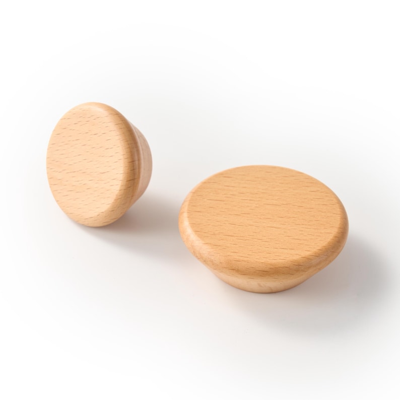Op de afbeelding: Twee ronde kastknoppen gemaakt van lichtgekleurd natuurlijk hout. Elke knop heeft een glad, afgerond bovenoppervlak met een zichtbaar houtnerfpatroon en een taps toelopende basis die naar het midden toe smaller wordt in een eenvoudig ontwerp.
