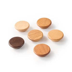 Op de afbeelding: Een verzameling van zes ronde houten kastknoppen gerangschikt in een groep. Elke knop heeft een glad, afgerond bovenoppervlak en een taps toelopende basis, met een verscheidenheid aan natuurlijke houtnerven en tinten vari&euml;rend van licht tot donkerbruin.