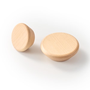 Op de afbeelding: Twee ronde houten knoppen in een lichtbruine kleur met zichtbare natuurlijke houtnerf. Elke knop heeft een glad, afgerond bovenoppervlak dat taps toeloopt naar een kleinere basis, wat zorgt voor een eenvoudig en functioneel ontwerp.