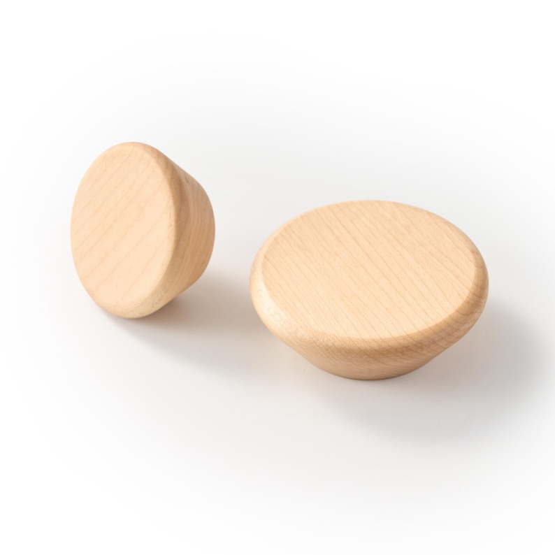 Op de afbeelding: Twee ronde houten knoppen in een lichtbruine kleur met zichtbare natuurlijke houtnerf. Elke knop heeft een glad, afgerond bovenoppervlak dat taps toeloopt naar een kleinere basis, wat zorgt voor een eenvoudig en functioneel ontwerp.