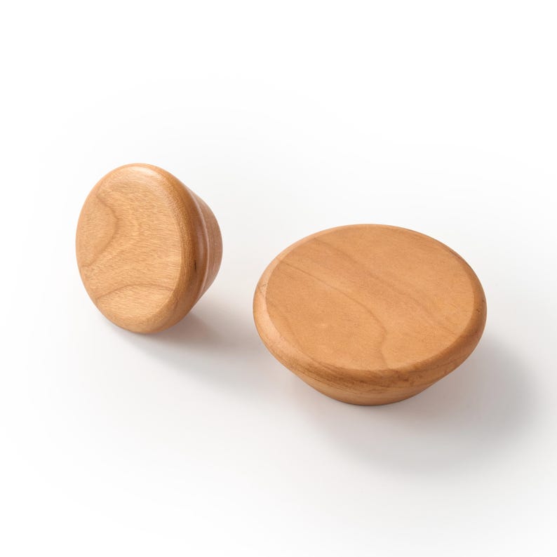 Op de afbeelding: Twee ronde houten knoppen met een gladde, lichtbruine afwerking en zichtbare natuurlijke houtnerfpatronen. De knoppen hebben een taps toelopende basis, waarbij de ene schuin staat en de andere plat ligt, wat hun cirkelvormige bovenzijden toont.