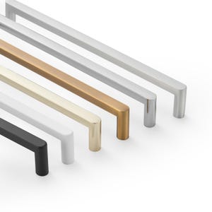 May include: A set of five linear cabinet pulls arranged in a diagonal row. The handles feature a smooth, rectangular profile with rounded edges, available in matte black, white, brushed gold, brass, and brushed silver metallic finishes.
