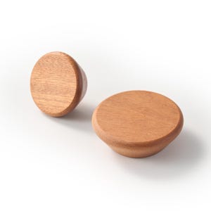 Op de afbeelding: Twee ronde houten knoppen met een gladde, lichtbruine afwerking en zichtbare houtnerf. Elke knop heeft een plat, afgerond bovenoppervlak dat taps toeloopt naar een kleinere basis, wat een natuurlijke textuur en warme houtkleur laat zien.