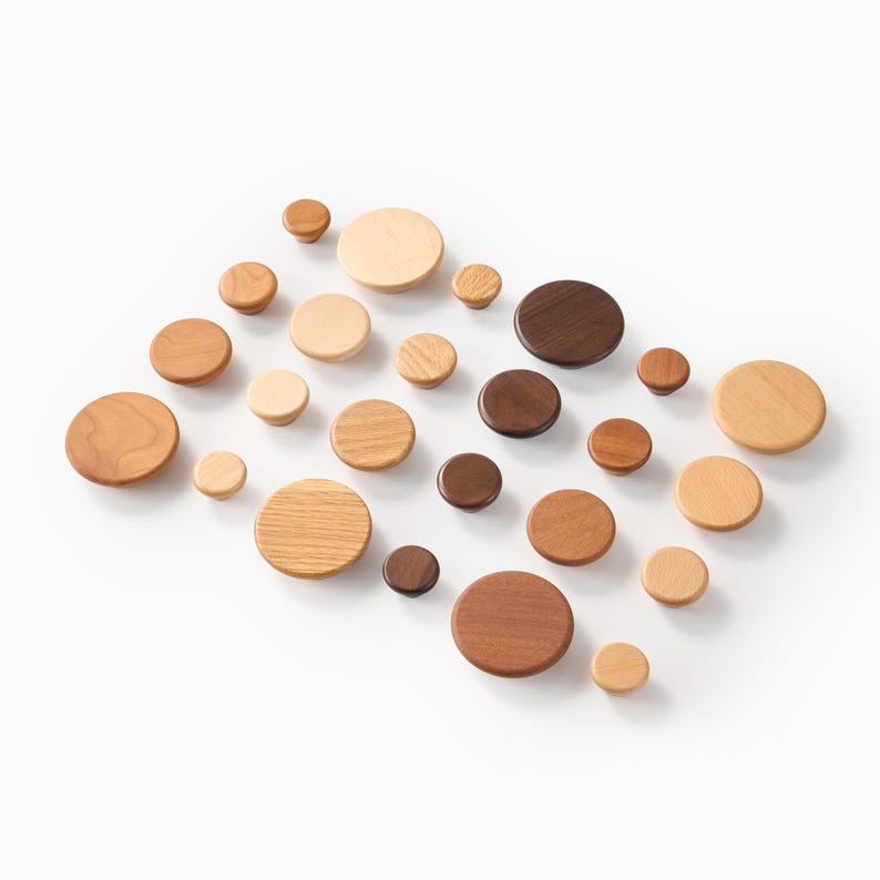 Op de afbeelding: Een verzameling van vierentwintig ronde houten knoppen gerangschikt in een raster. De knoppen vari&euml;ren in grootte en hebben verschillende houttinten, vari&euml;rend van lichtbeige en middenbruin tot donker espresso, met natuurlijke houtnerven.