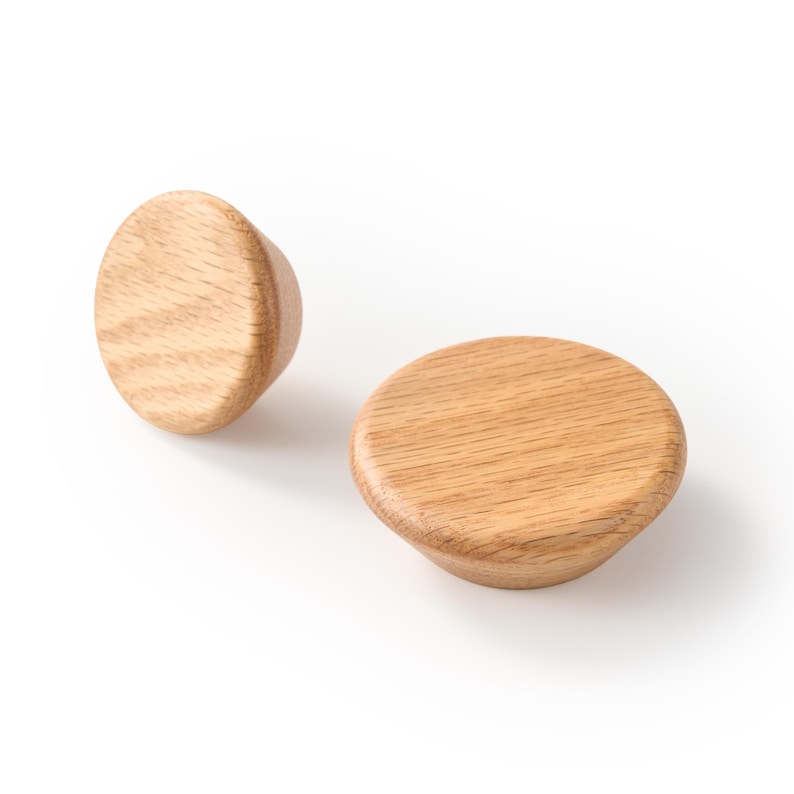 Op de afbeelding: Twee ronde houten knoppen met een natuurlijke lichtbruine afwerking en zichtbare houtnerfpatronen. Elke knop heeft een plat, afgerond bovenoppervlak dat taps toeloopt naar een kleinere basis, wat de organische textuur van het houtmateriaal toont.