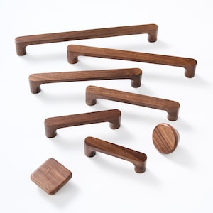 May include: A collection of dark brown wooden cabinet hardware including five rectangular bar pulls of varying lengths, one circular knob, and one square knob with rounded corners, all featuring a smooth finish and visible wood grain patterns.