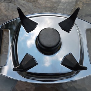 May include: A silver serving tray with four black, pointed supports and a black, round center piece. The tray has two black handles.