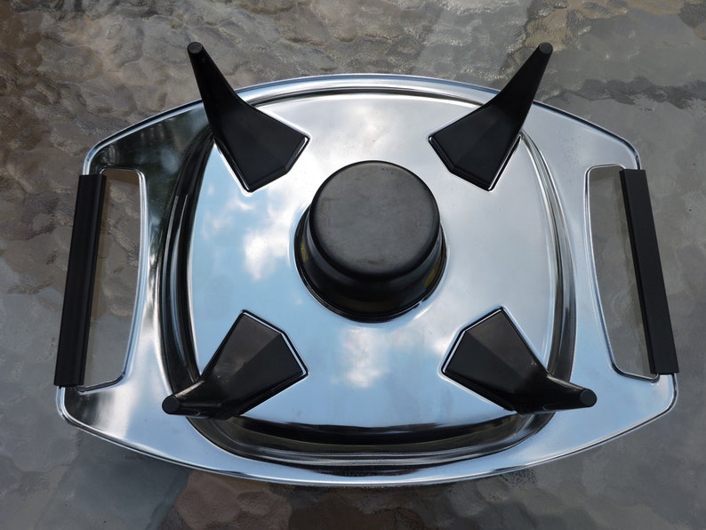 May include: A silver serving tray with four black, pointed supports and a black, round center piece. The tray has two black handles.