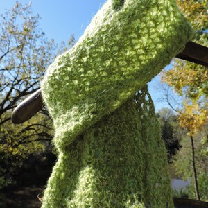 May include: A green crocheted scarf with a delicate openwork pattern and small green beads. The scarf is draped over a metal hook.