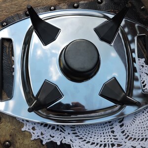 May include: A silver serving tray with four black triangular handles. The tray has a round, black center piece.
